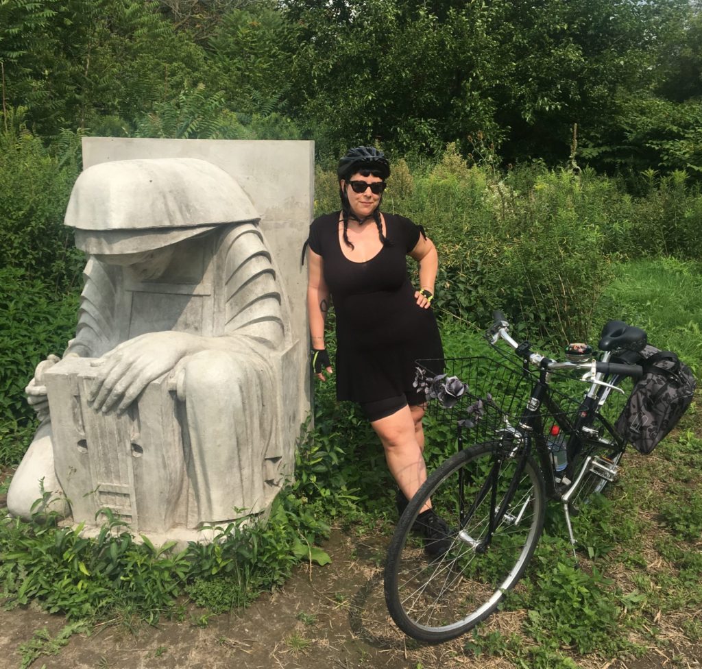 Women stops while cycling in Toronto to pose with Gargoyle sculpture on the Don River Valley bike trail